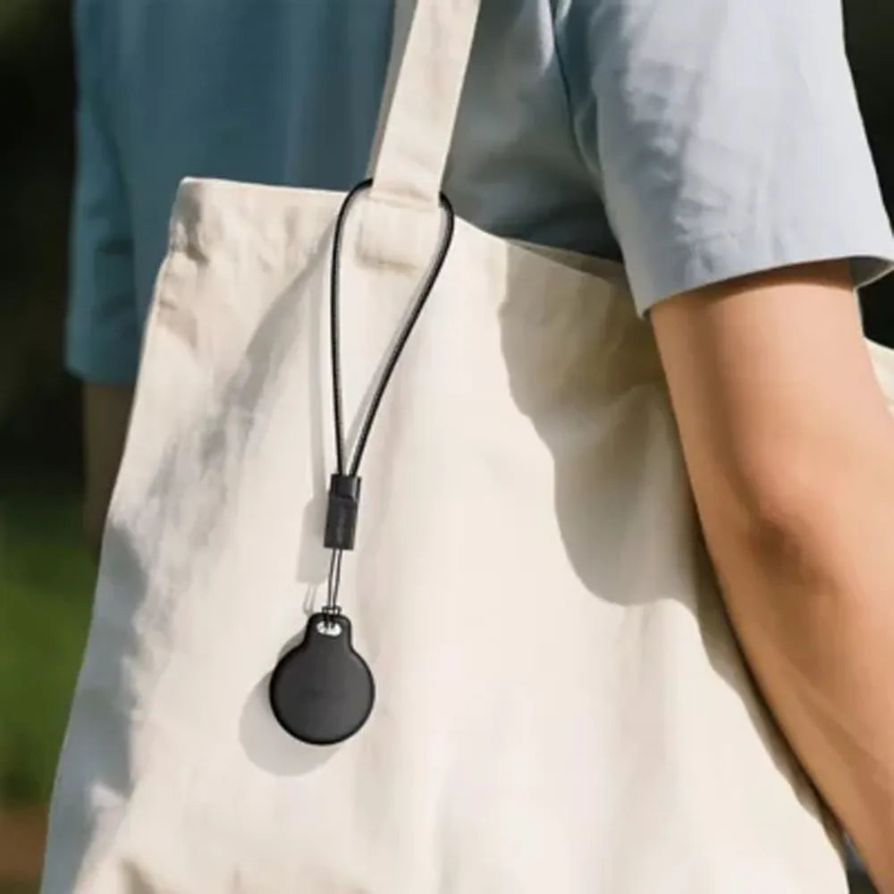 Black lanyard with round device attached to a beige bag held by a person.