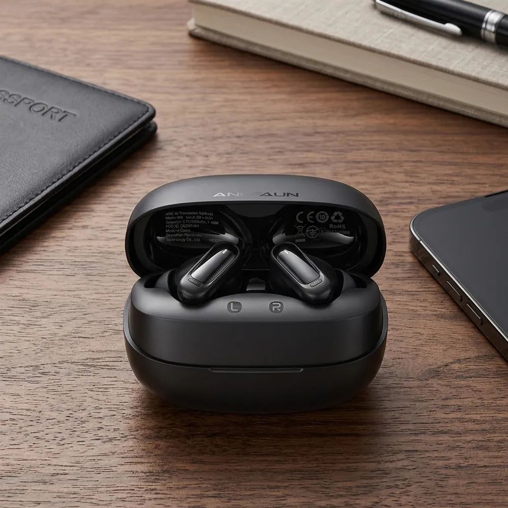 Black wireless earbuds in an open charging case on a wooden desk, surrounded by a notebook, pen, phone, and passport cover.