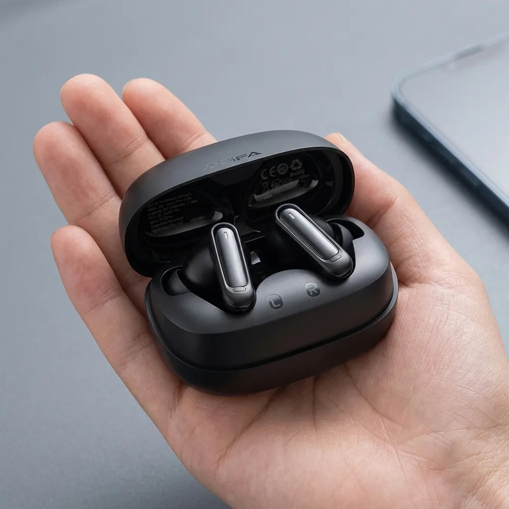 A hand holding an open black wireless earbud charging case with two earbuds inside, photographed against a smooth gray surface.