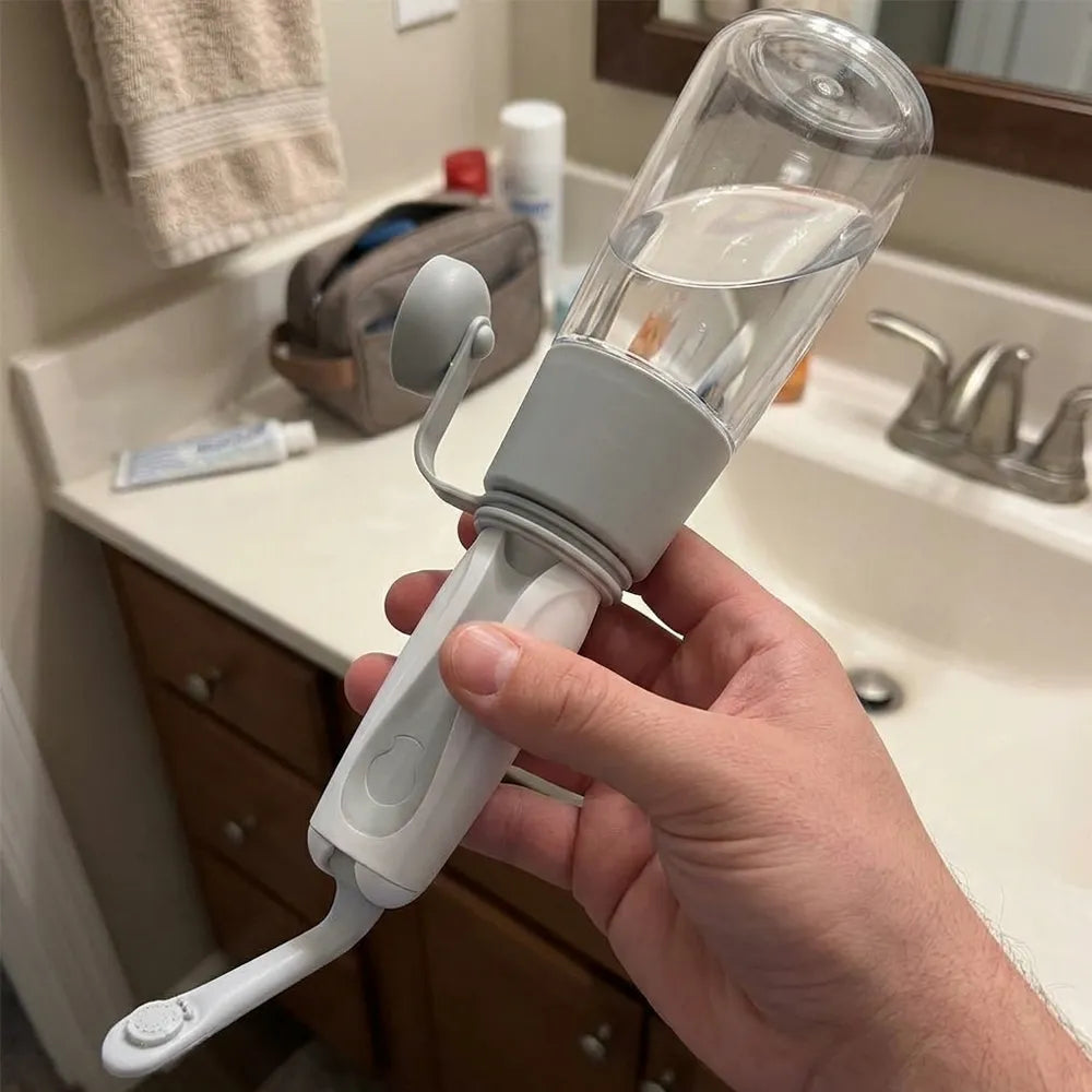 A hand holding a white and gray oral irrigator water flosser with a clear plastic reservoir, shown in a bathroom setting with a sink and toiletries in the background.