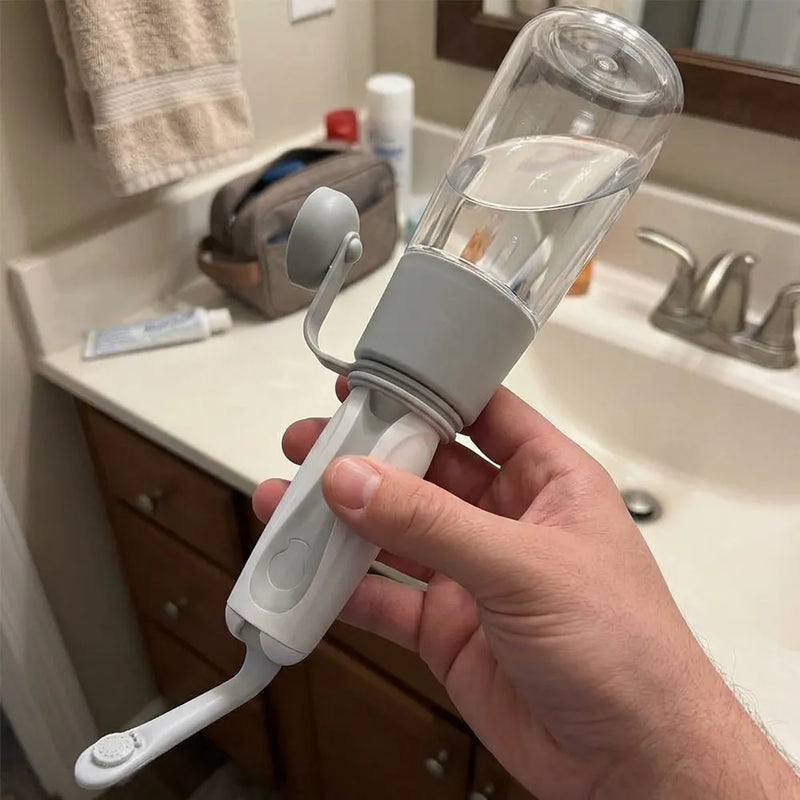 A hand holding a white and gray oral irrigator water flosser with a clear plastic reservoir, shown in a bathroom setting with a sink and toiletries in the background.