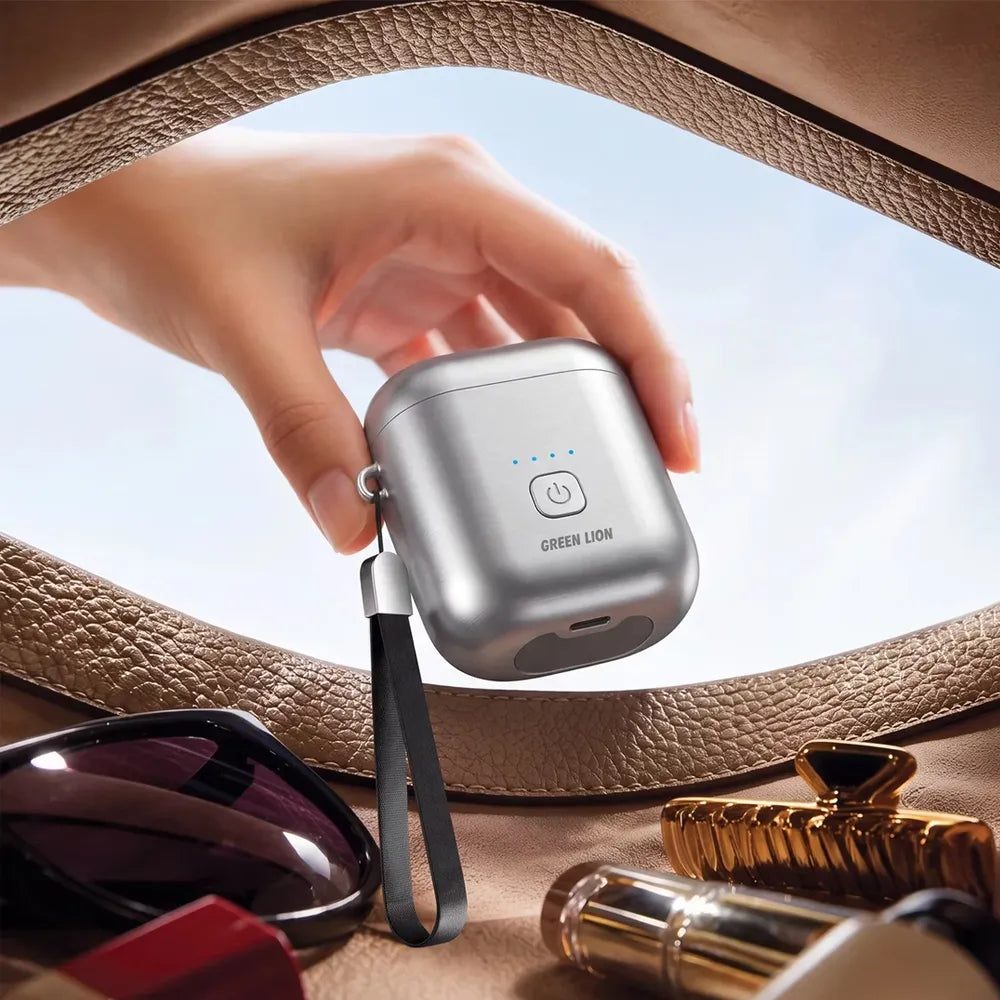A hand holds a silver wireless earbud charging case with a black wrist strap and blue LED indicator lights. The case has the text 'GREEN LION' printed on the front.