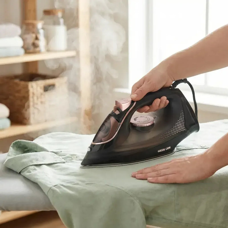 A person ironing a light green shirt on a white ironing board, using a modern black steam iron with rose gold accents.