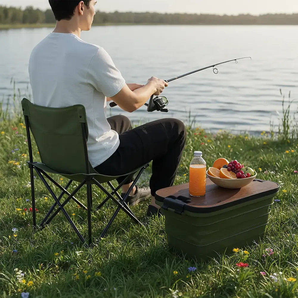 Person fishing by a lake with a portable chair and food on a table.