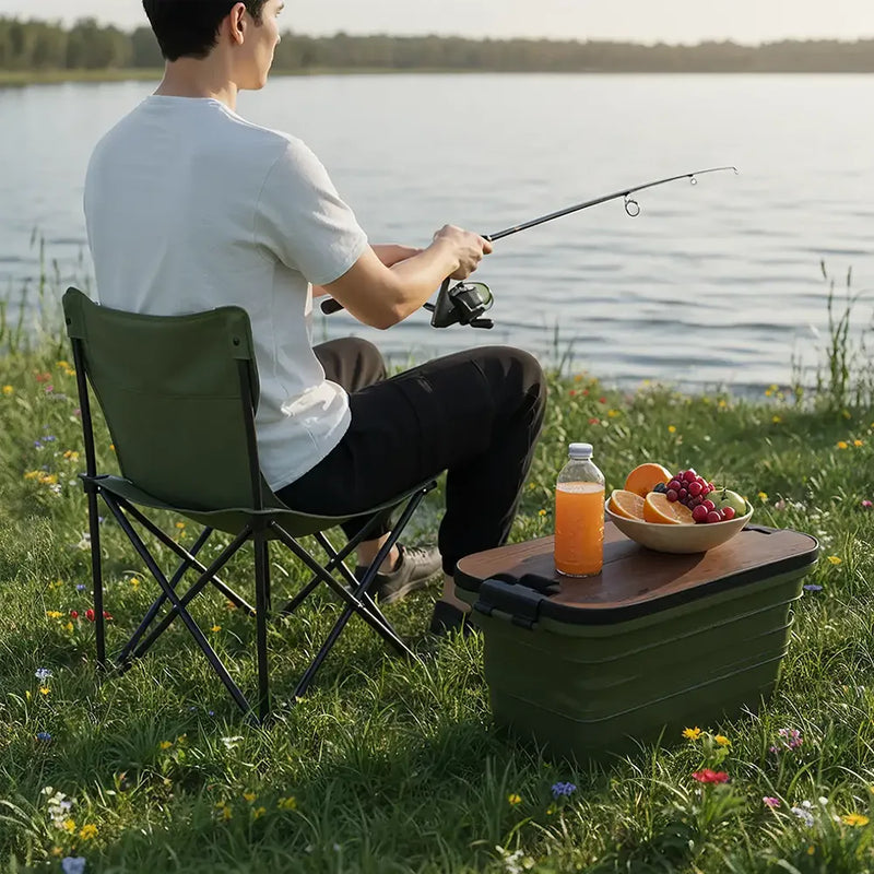 Person fishing by a lake with a portable chair and food on a table.