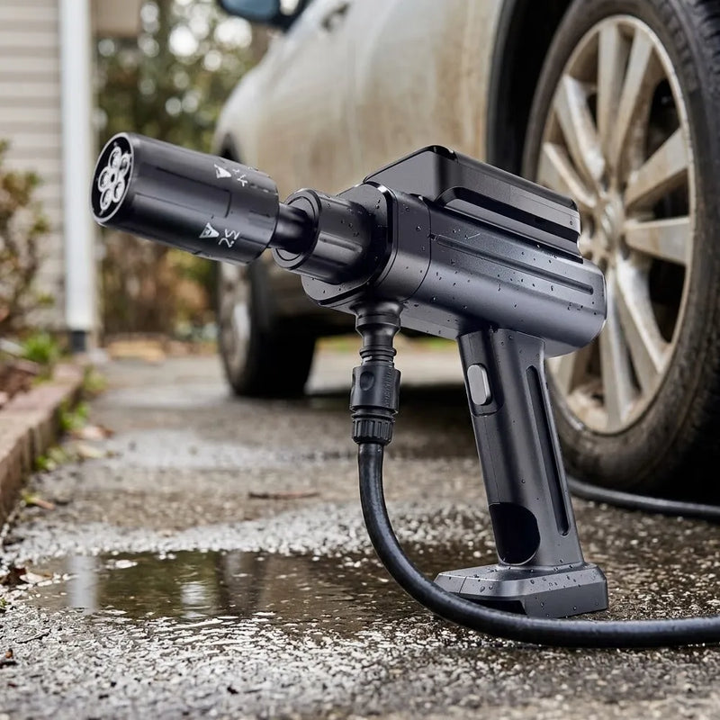 A black electric pressure washer connected to a hose, positioned outdoors on wet pavement next to a car wheel.