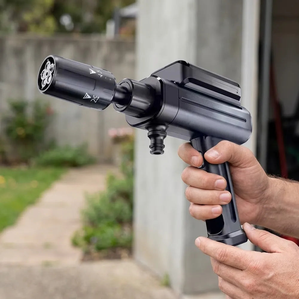 A person's hands holding a black handheld pressure washer nozzle outdoors in front of a blurred concrete wall and garden path.