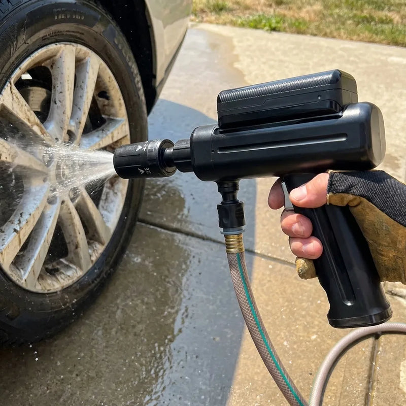 A black handheld high-pressure car tire cleaner spray gun being used to wash a dirty car wheel outdoors on a concrete driveway.