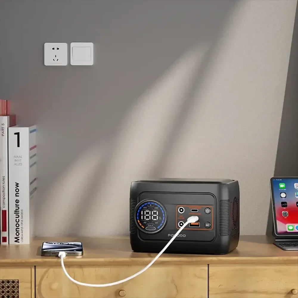 Portable power station on a wooden surface with a phone and other devices connected, against a neutral wall.