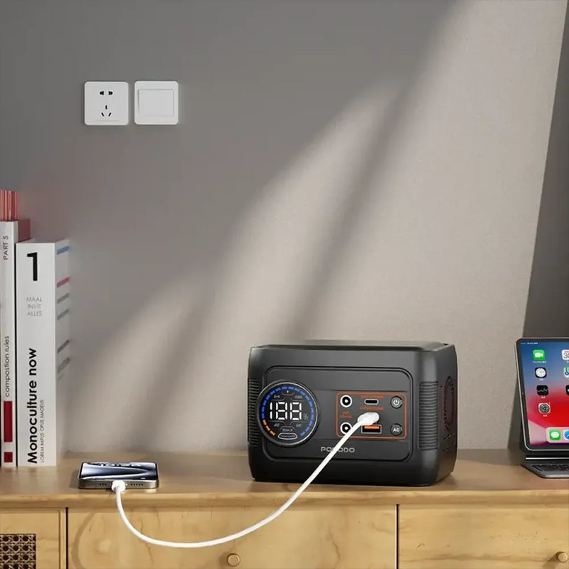 Portable power station on a wooden surface with a phone and other devices connected, against a neutral wall.