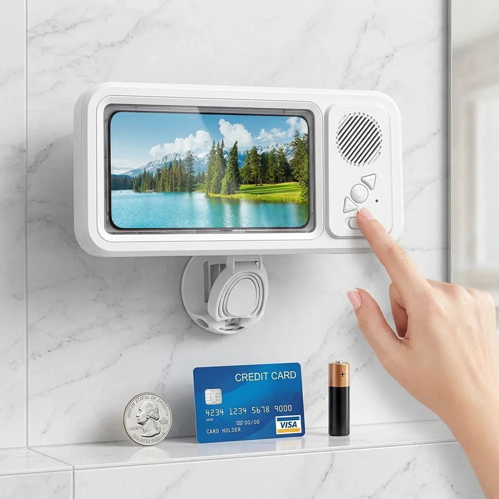 A white wall-mounted electronic device with a screen showing a lake landscape and control buttons on the right, mounted on a marble bathroom wall. A hand is touching the buttons, and a credit card and coin are placed below for scale.